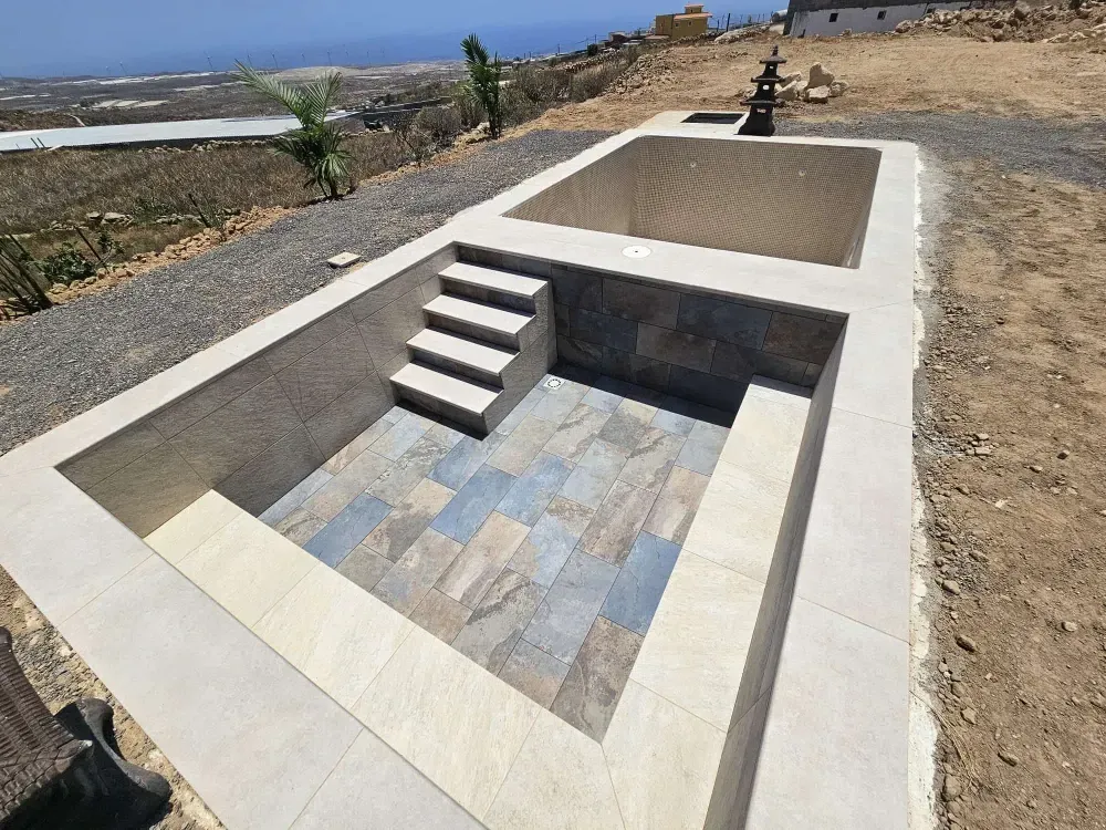 Piscina exterior de dos partes: una con escalones y suelo de baldosas, y la otra vacía. 