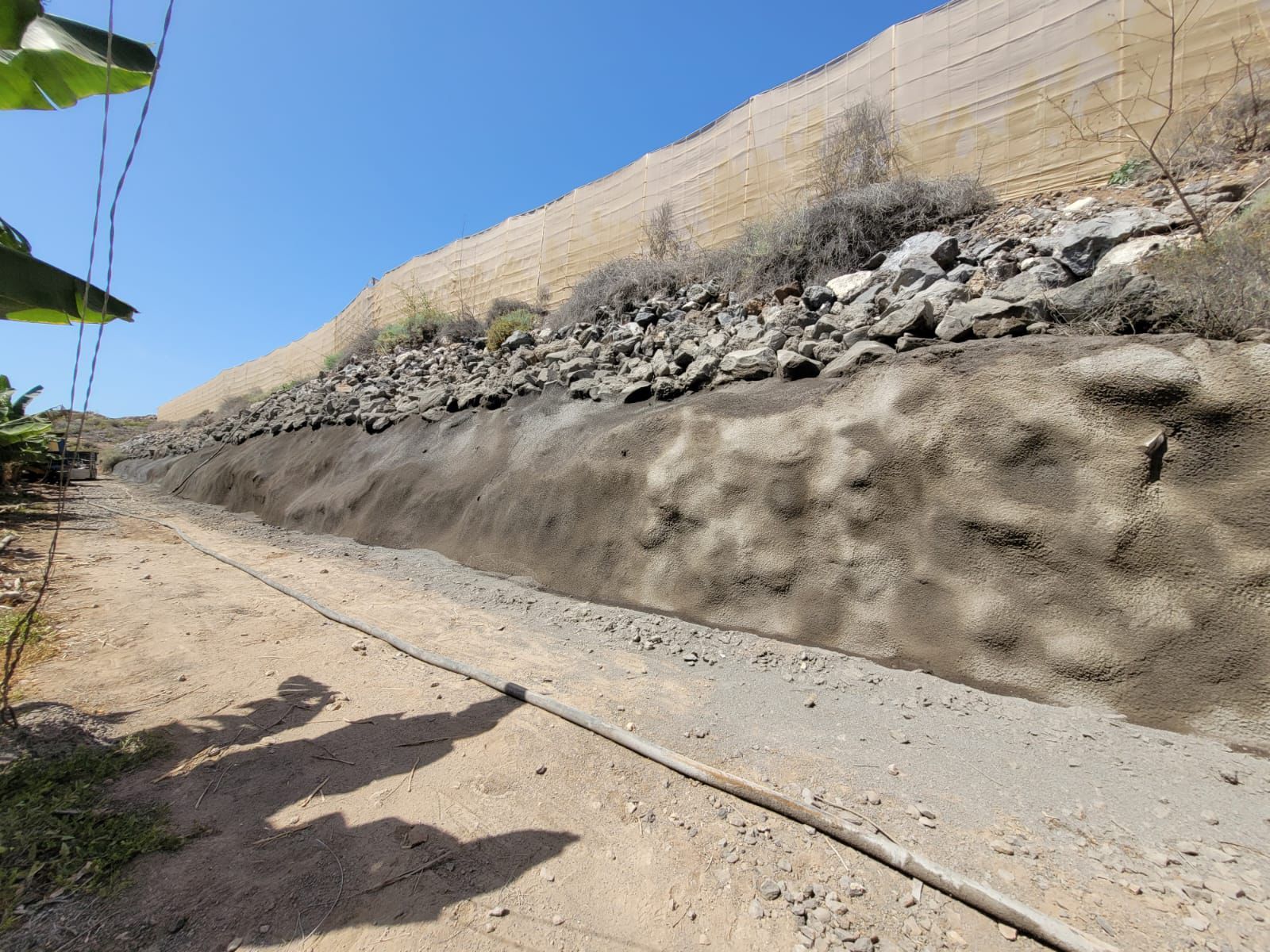 Un camino de tierra que corre a lo largo de un muro de contención construido con rocas y tierra