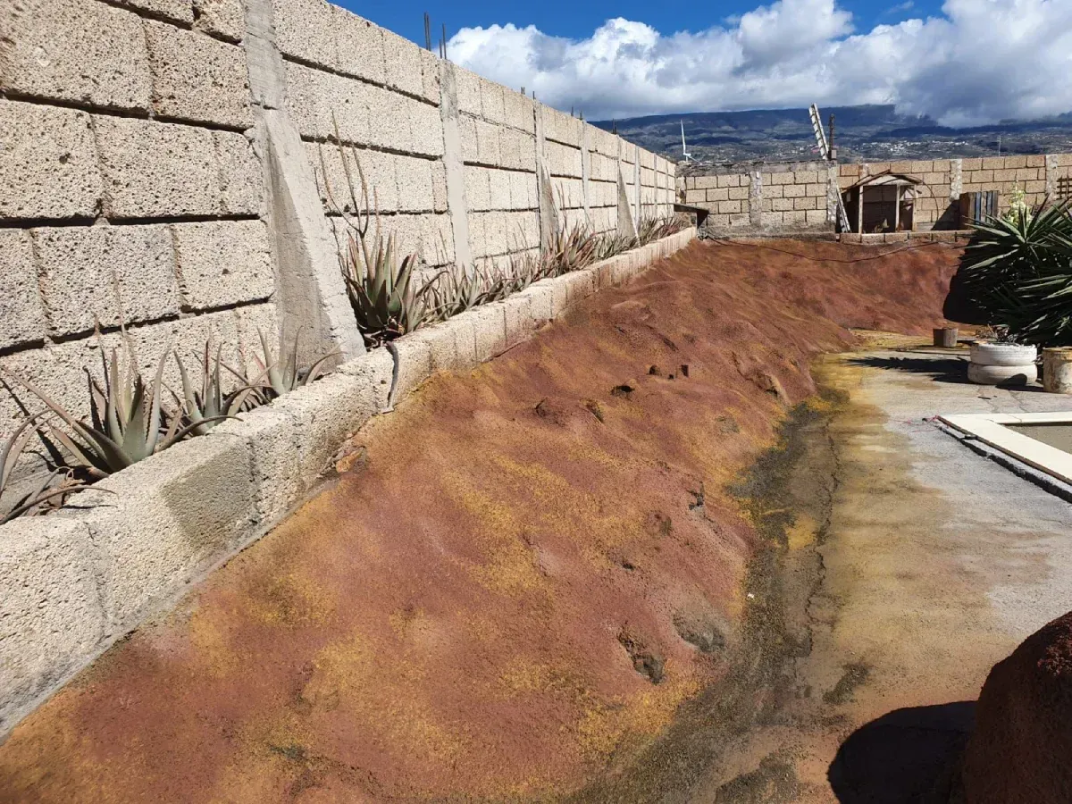 Un lecho largo y elevado con tierra rojiza y una pared de ladrillos