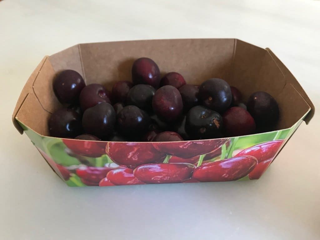 Un recipiente de cartón lleno de cerezas sobre una mesa.