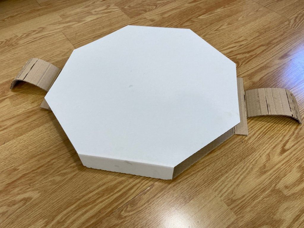 Una caja blanca en forma de octágono se encuentra sobre un piso de madera.