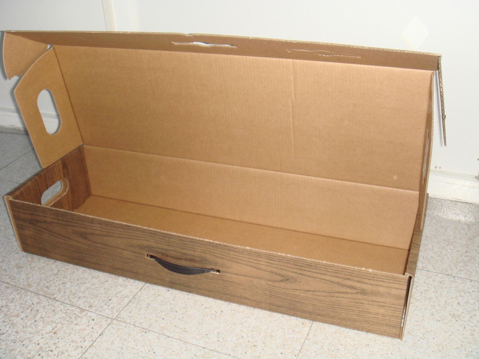 Una caja de cartón vacía con asa reposa sobre un suelo de baldosas.