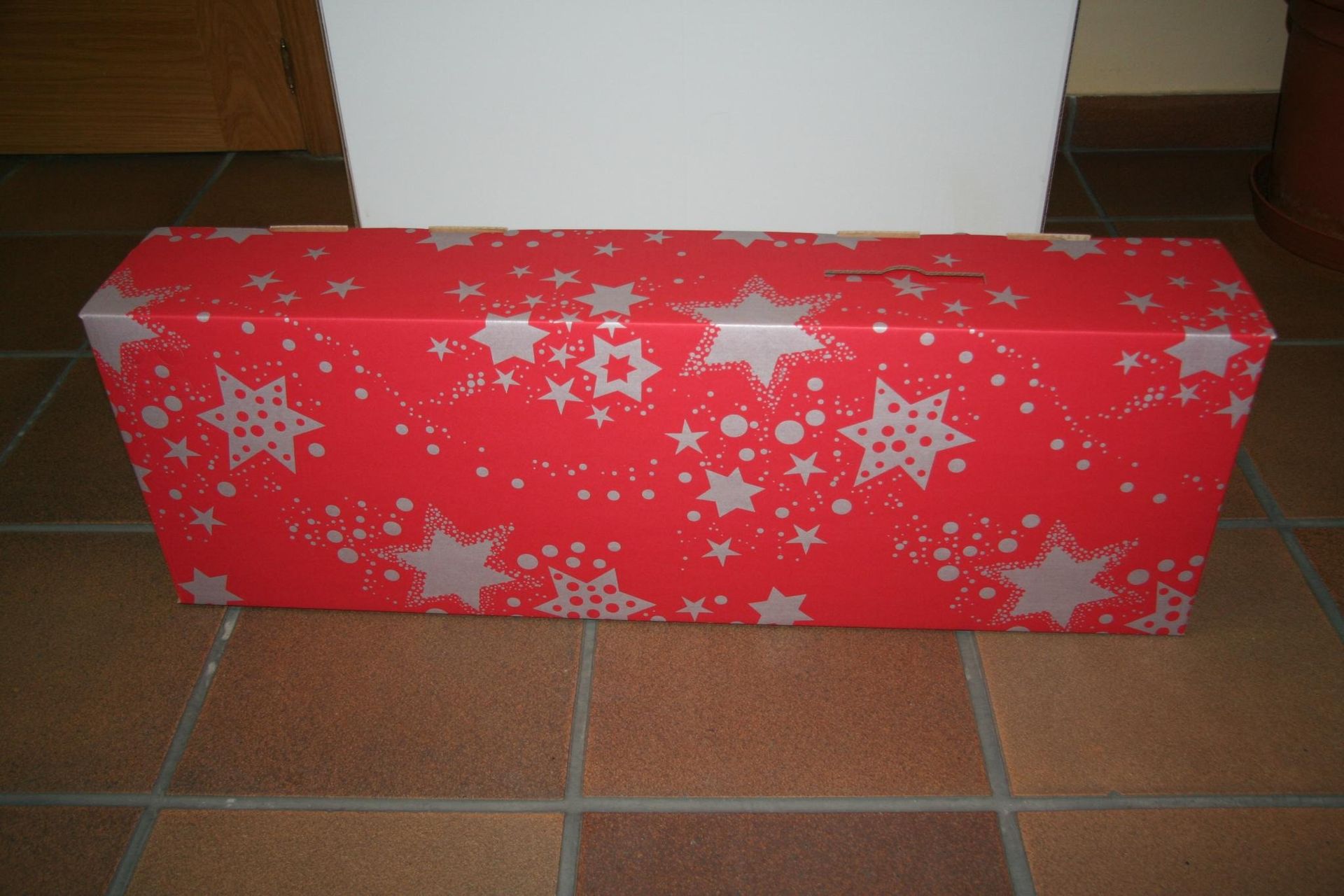Una caja roja con estrellas plateadas reposa sobre un suelo de baldosas.