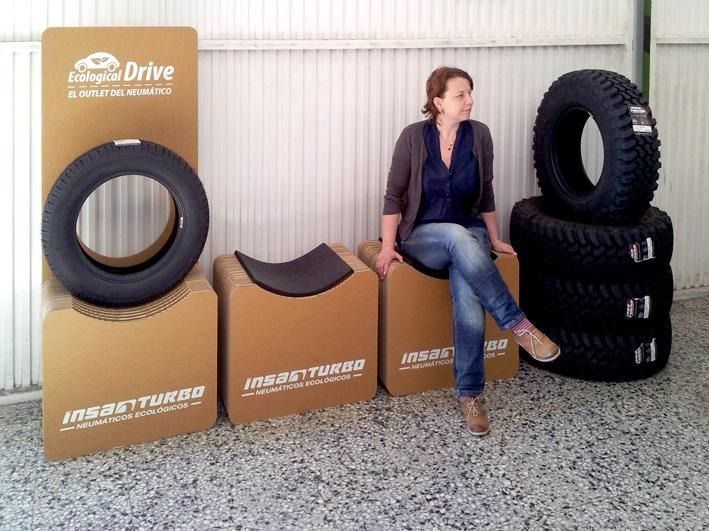 Una mujer se sienta en una silla de cartón junto a una pila de neumáticos.