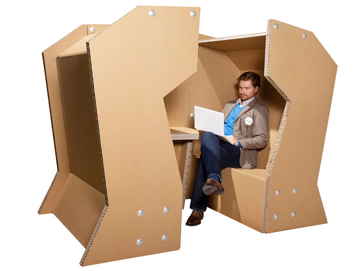 Un hombre está sentado en una caja de cartón con una computadora portátil.