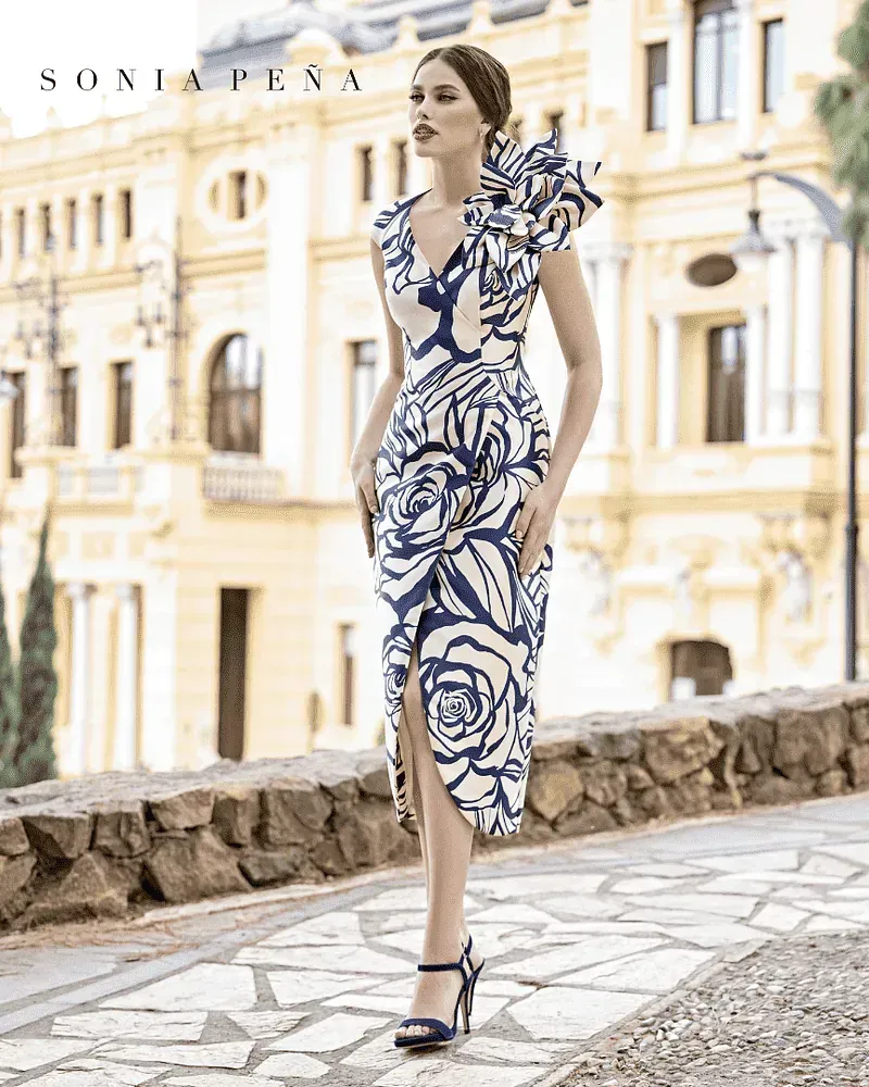 Una mujer con un vestido azul y blanco está parada frente a un edificio.