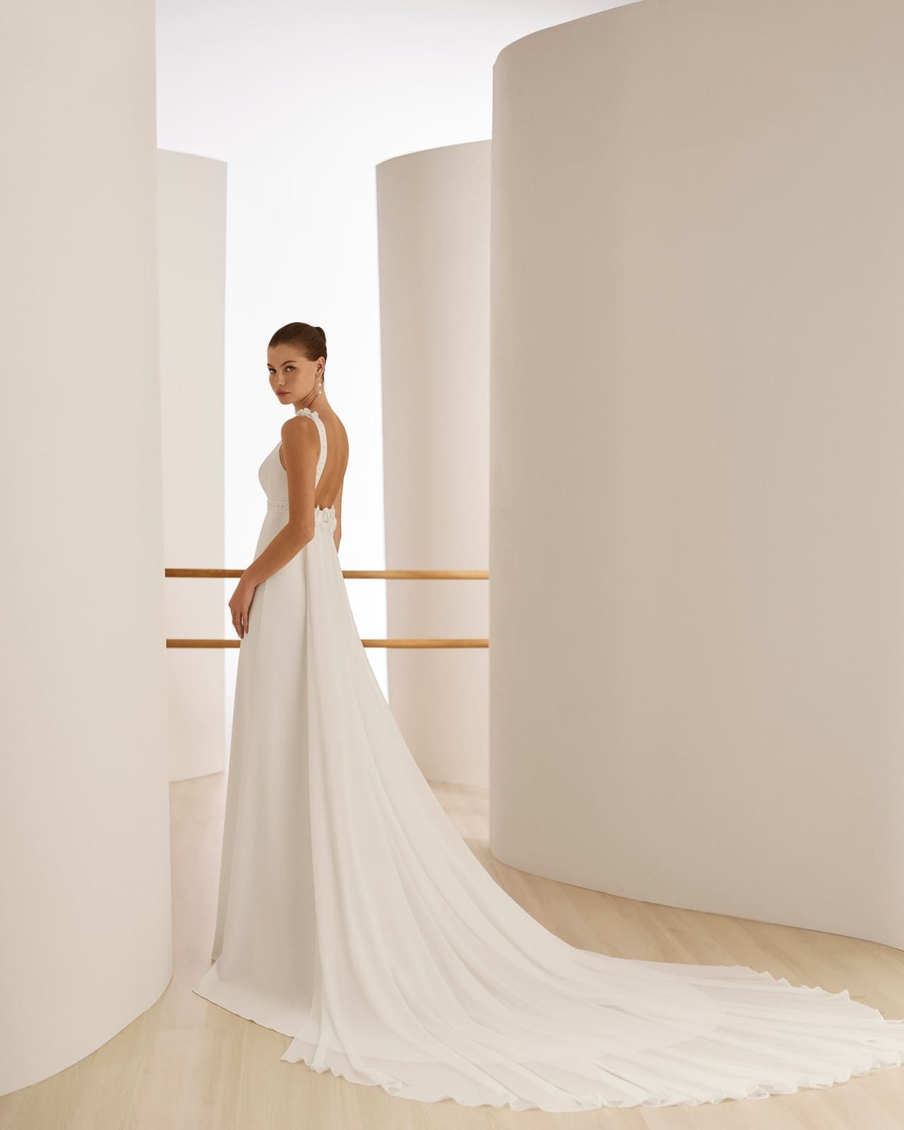 Novia con vestido blanco de larga cola de pie en un luminoso salón minimalista.