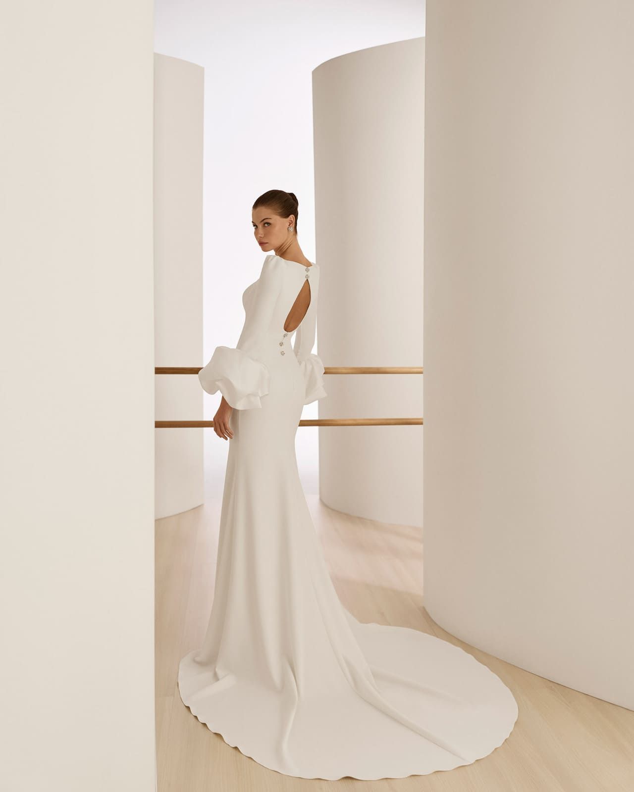 Mujer con un vestido blanco de larga cola, de pie en un pasillo luminoso y minimalista.