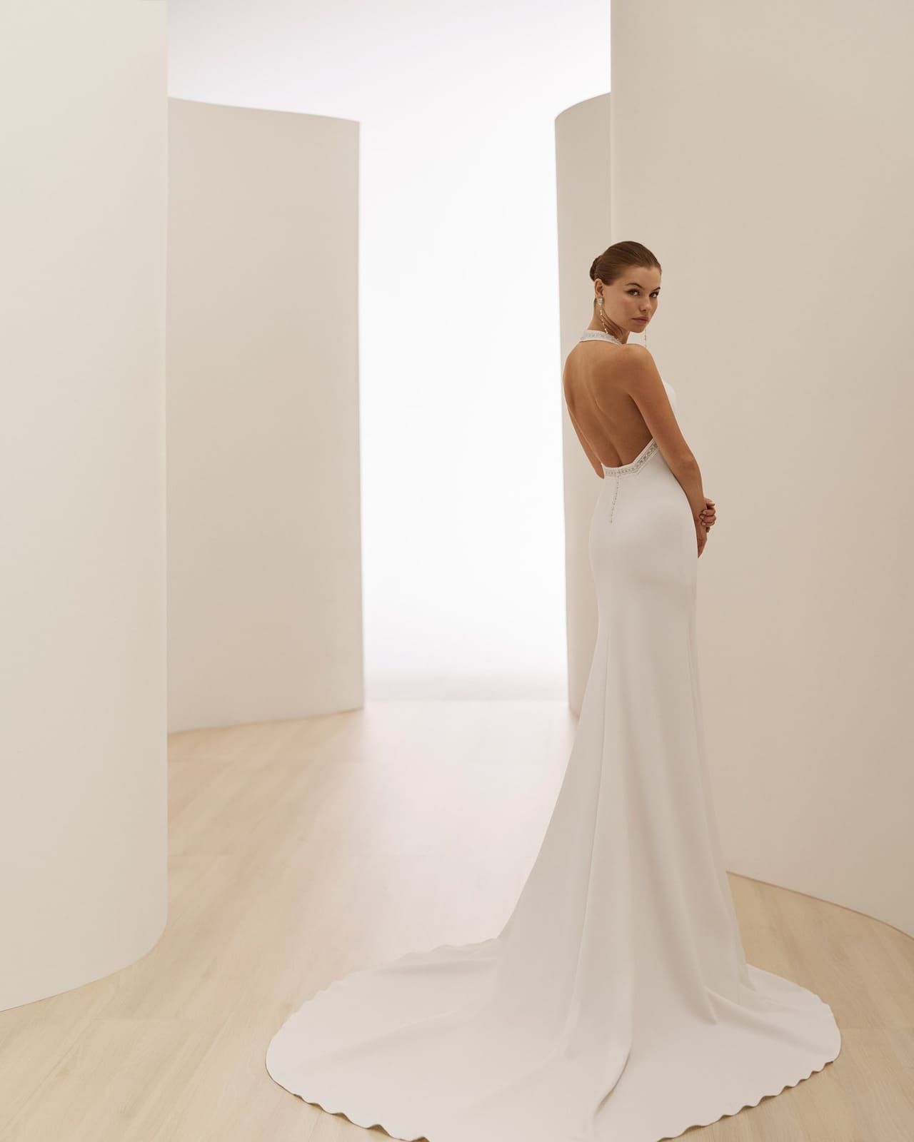 Mujer con vestido blanco sin espalda de pie en un pasillo luminoso y minimalista.