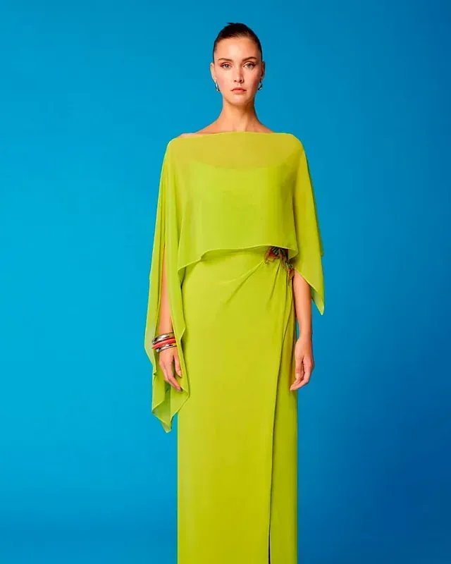 Una mujer lleva un vestido largo verde con una capa.