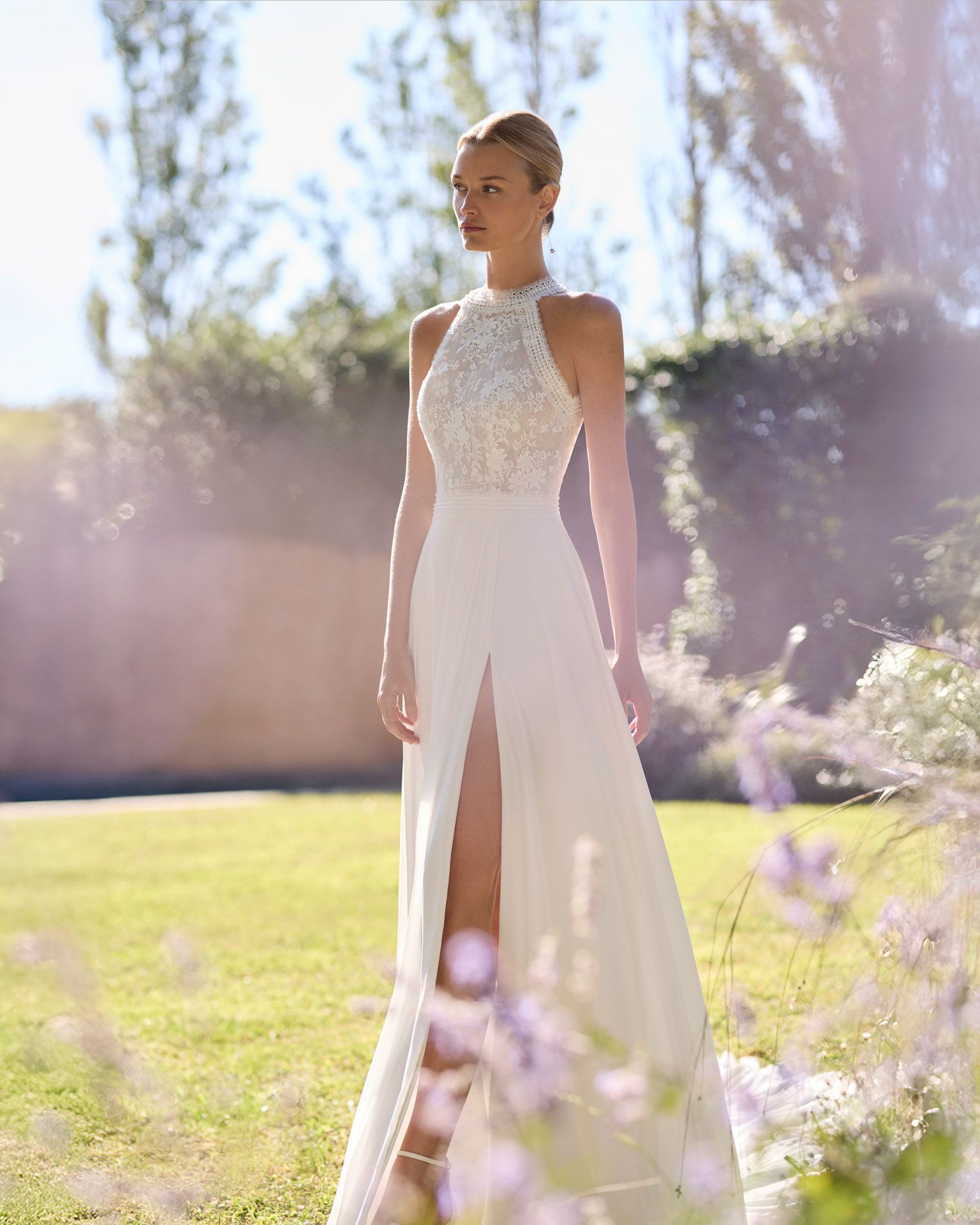 Novia con un vestido de encaje blanco, de pie al aire libre en un jardín soleado.