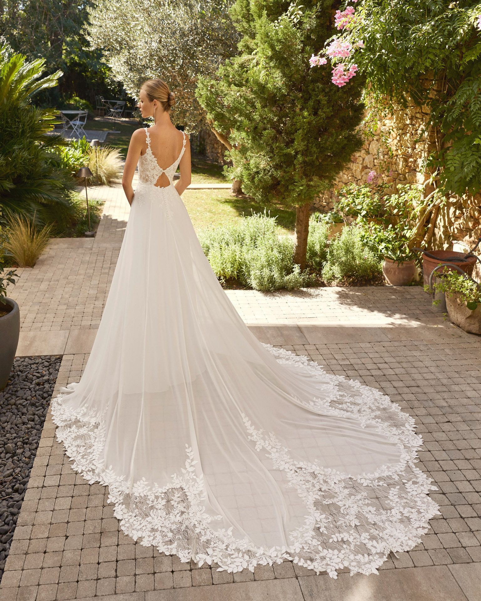 Novia con un vestido blanco de encaje con una larga cola, de pie en un sendero del jardín.