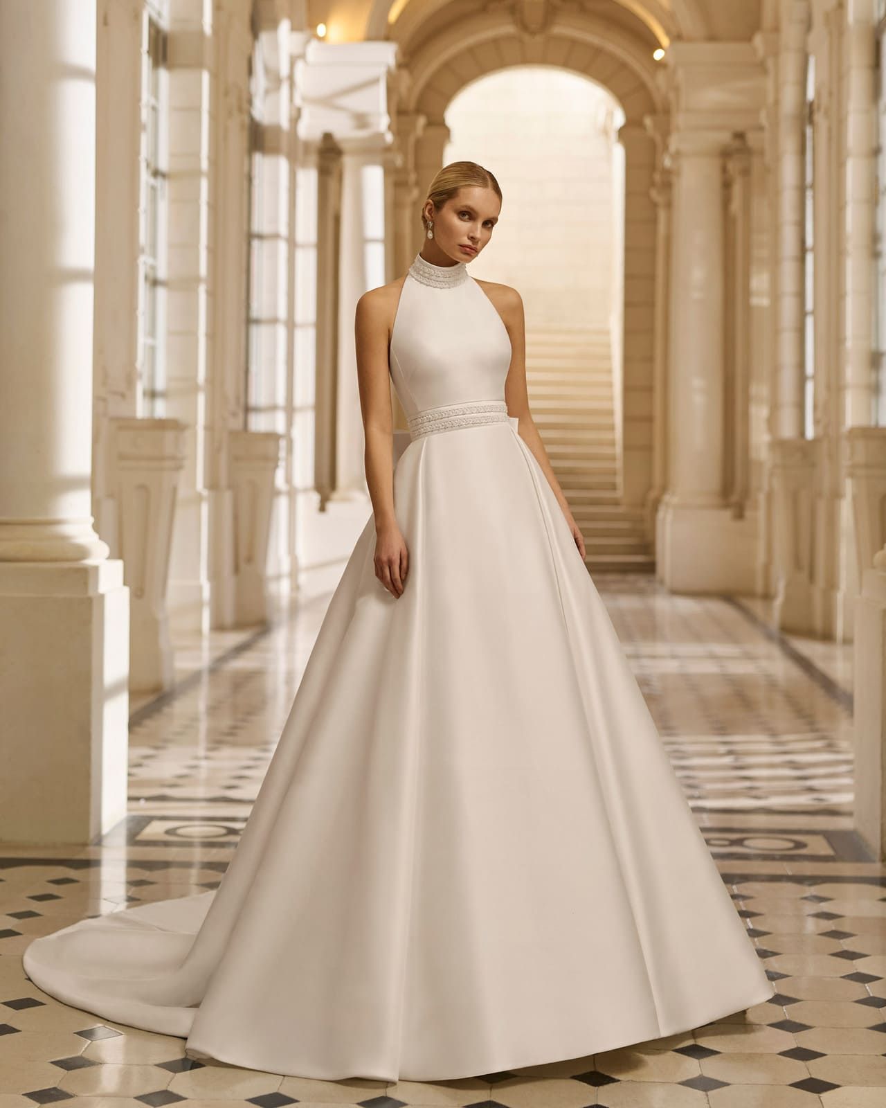 Modelo con un vestido blanco sin mangas de pie en un elegante pasillo arqueado.