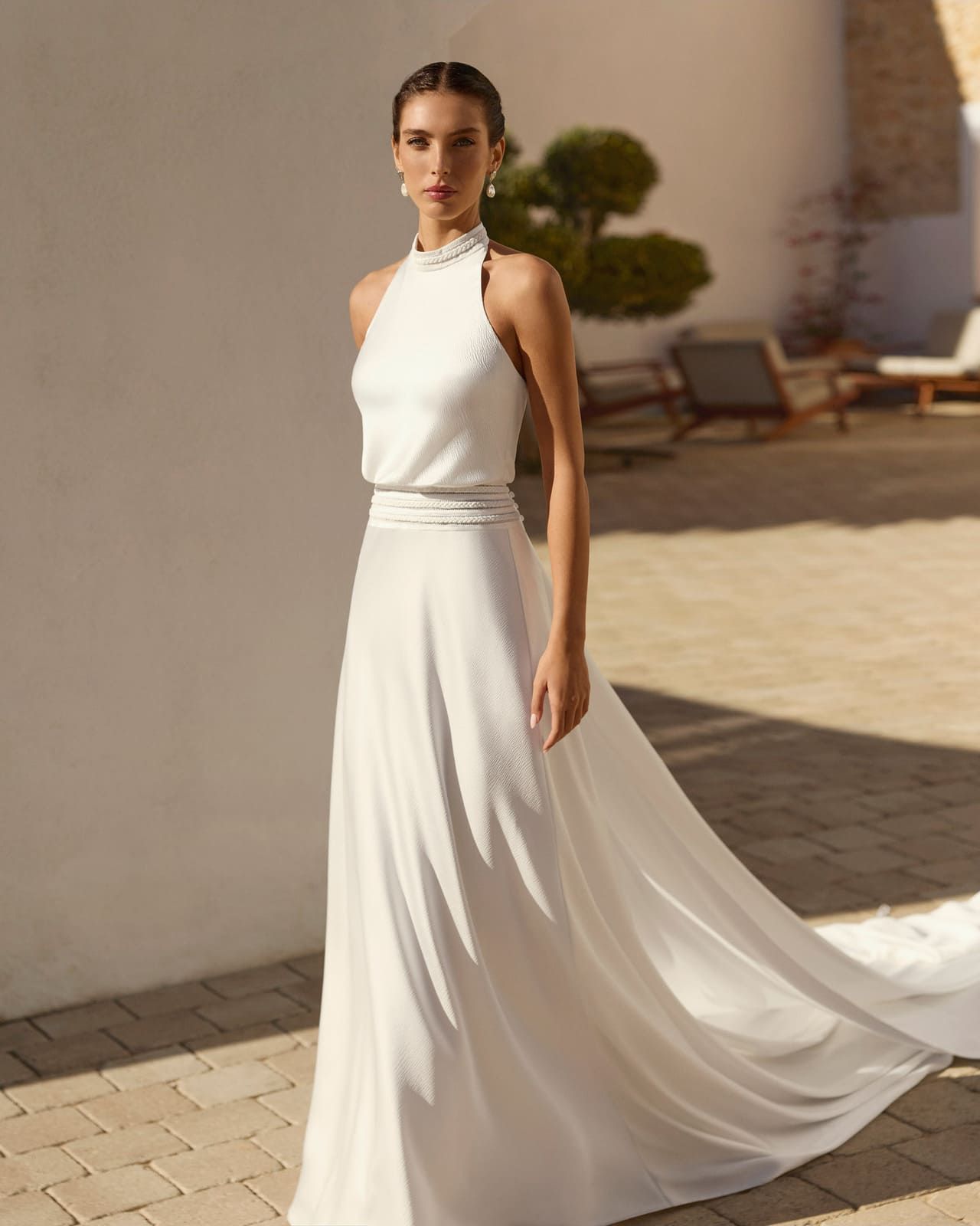 Mujer con vestido blanco de tirantes, de pie al aire libre en un patio soleado.