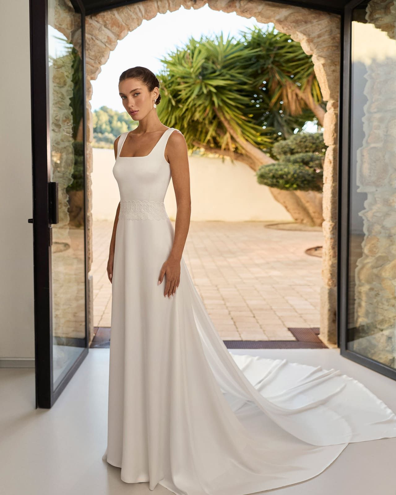Novia con un vestido de novia blanco de pie en una puerta con una larga cola al aire libre