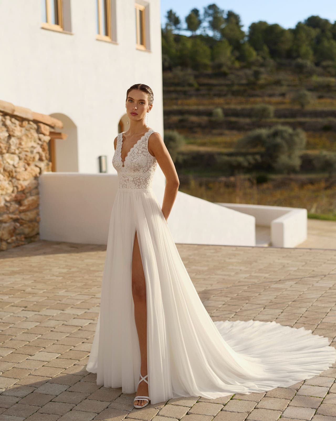 Mujer con un vestido de novia blanco de larga cola, de pie al aire libre en una terraza soleada.