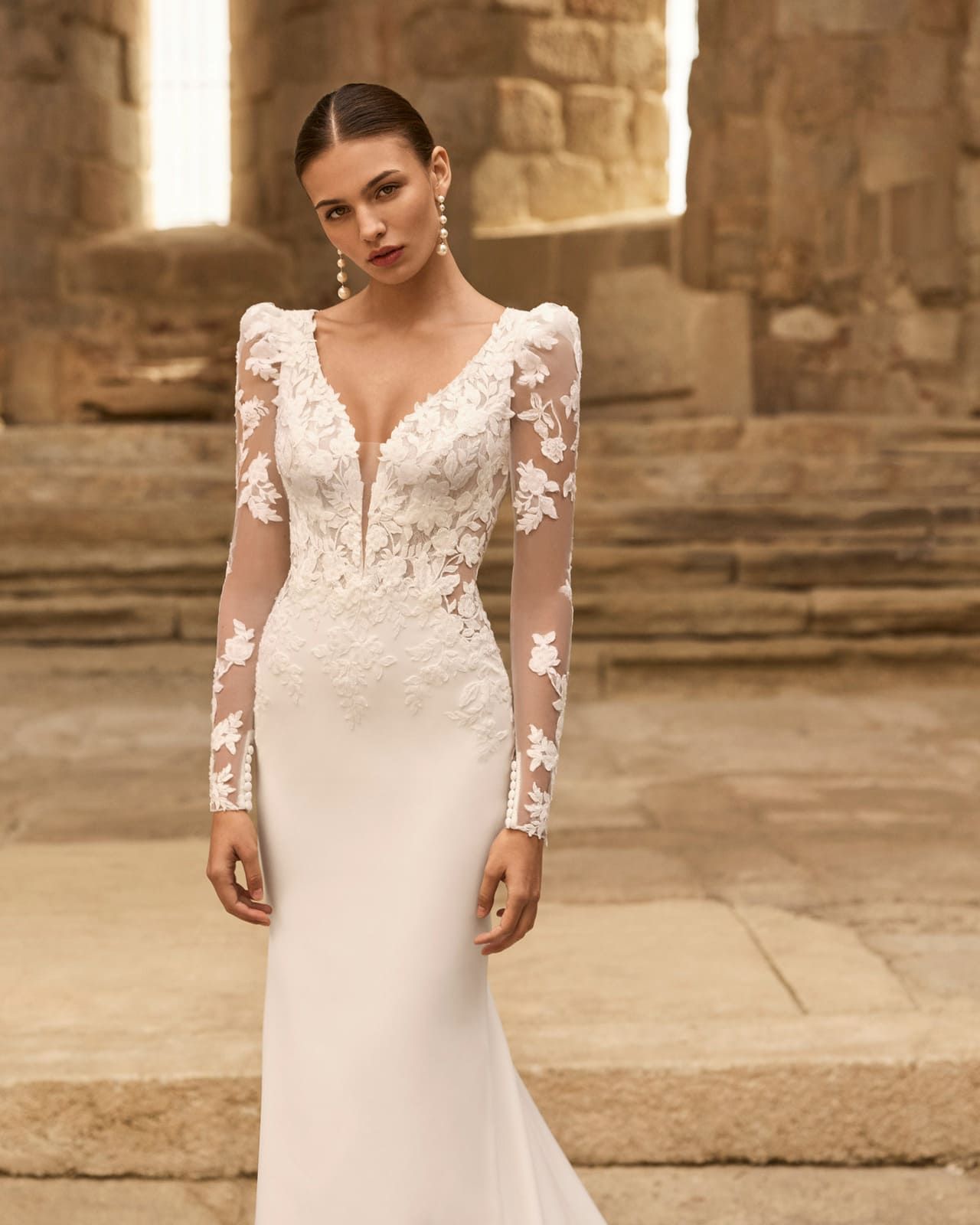 Mujer con vestido de novia de encaje blanco de pie en un patio de piedra.