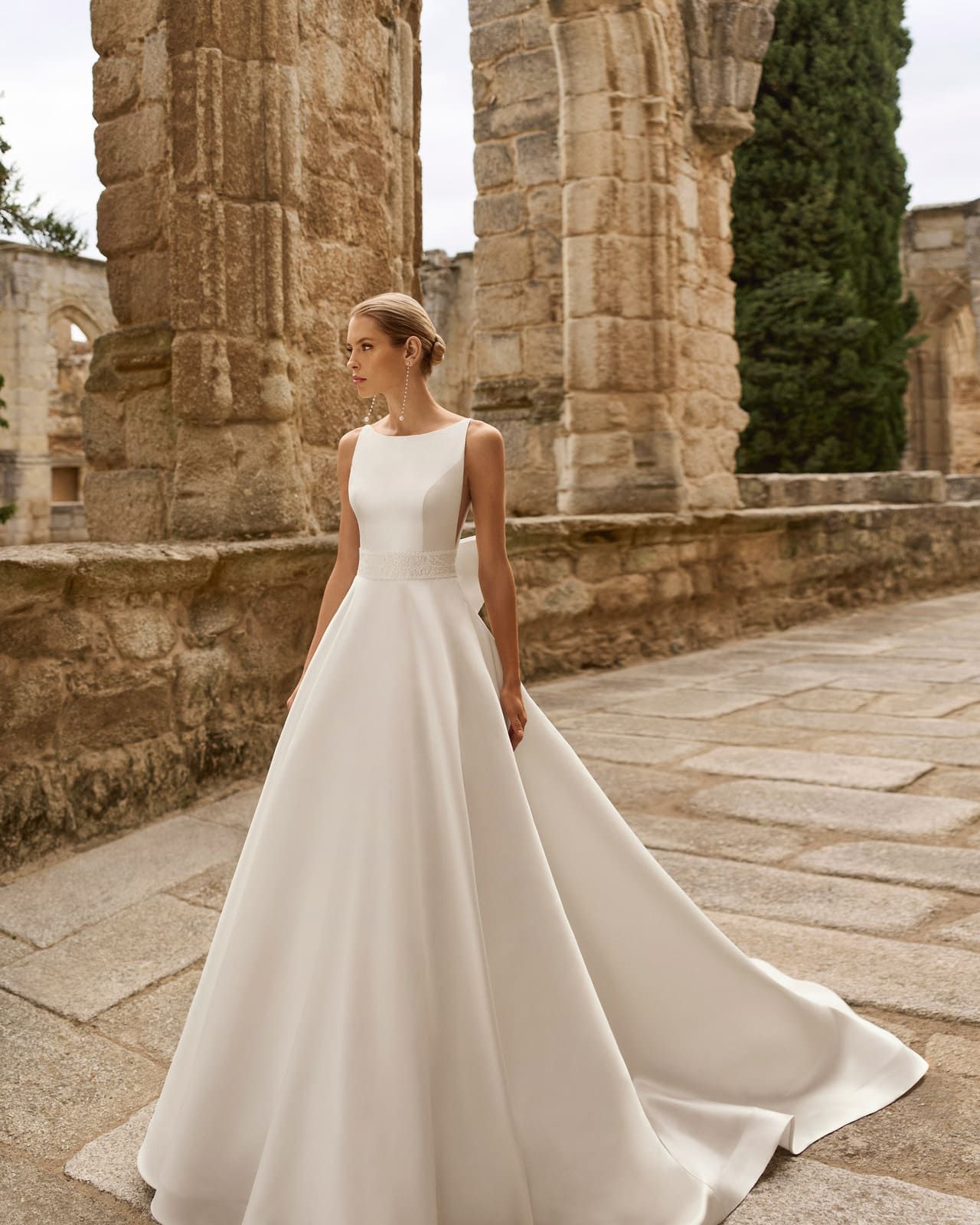 Mujer con un vaporoso vestido blanco de pie entre antiguas ruinas de piedra.