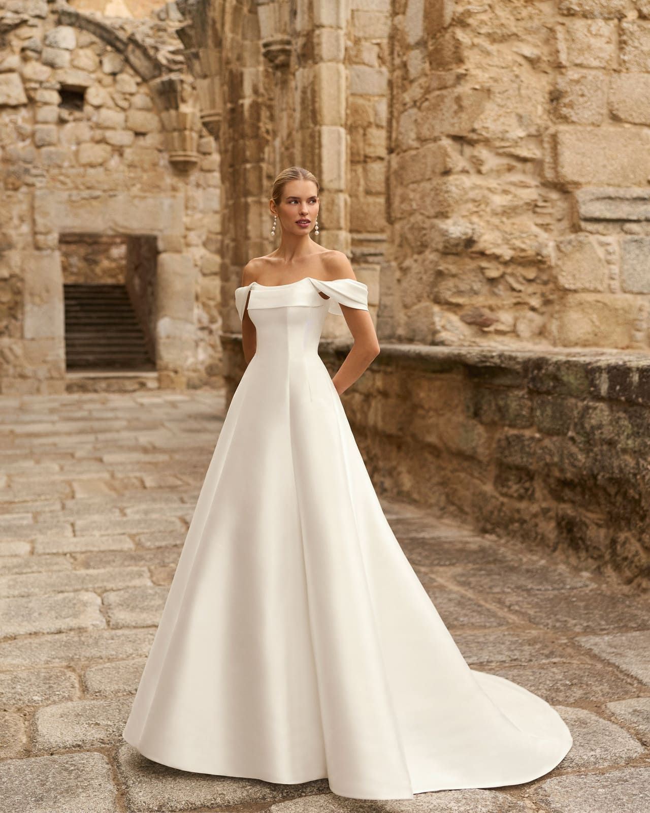 Mujer con un vestido blanco sin hombros de pie en un patio de piedra.
