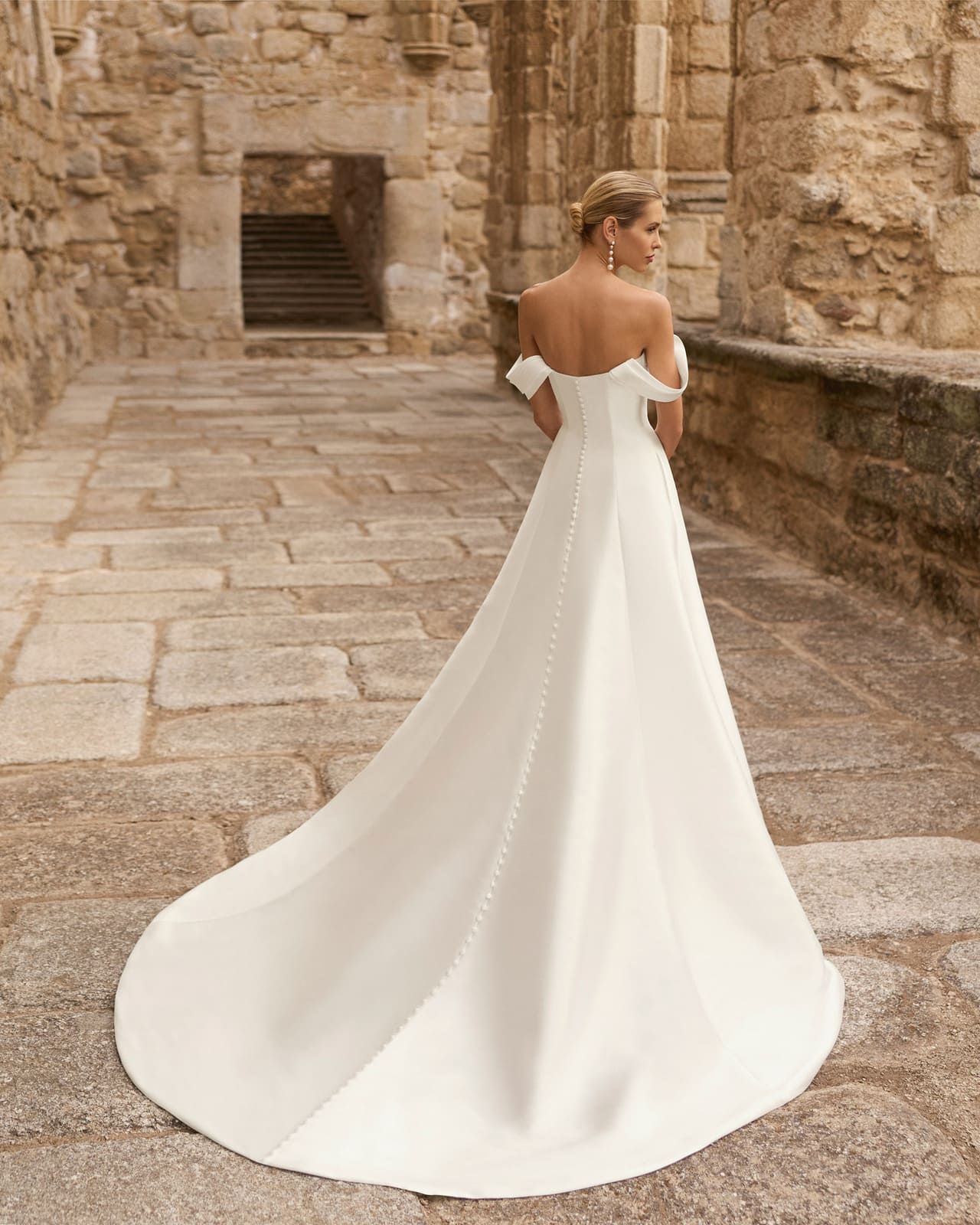 Mujer con un vaporoso vestido blanco caminando por un sendero de piedra en un patio histórico.