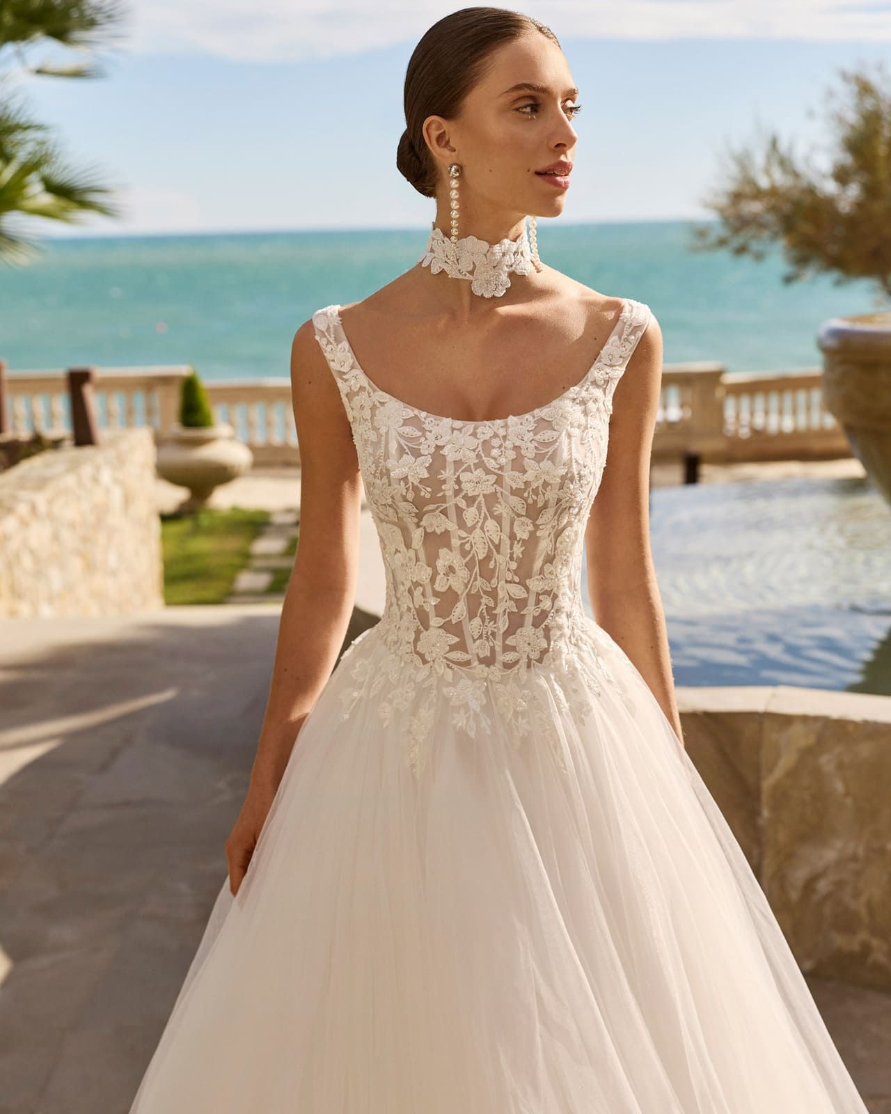 Mujer con un vestido de novia de encaje blanco de pie junto al mar al atardecer.