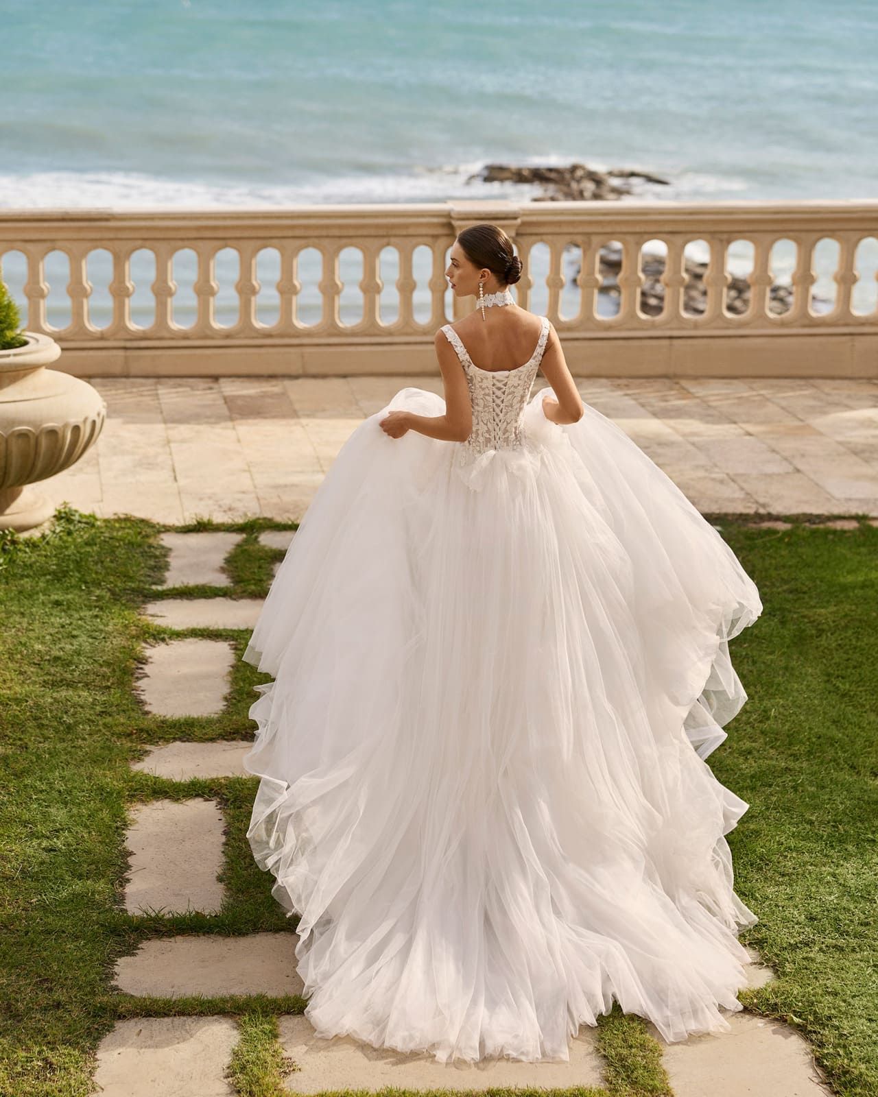Novia con vestido blanco de pie en una terraza con vistas al océano.
