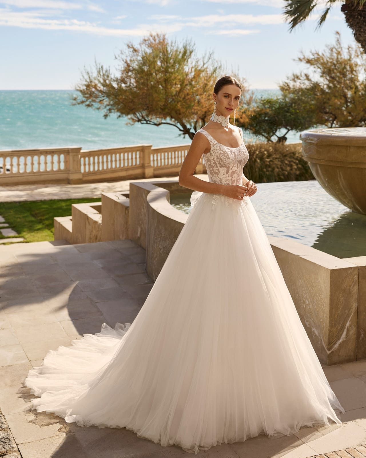 Novia con vestido de novia blanco de pie junto al mar en una terraza al aire libre.