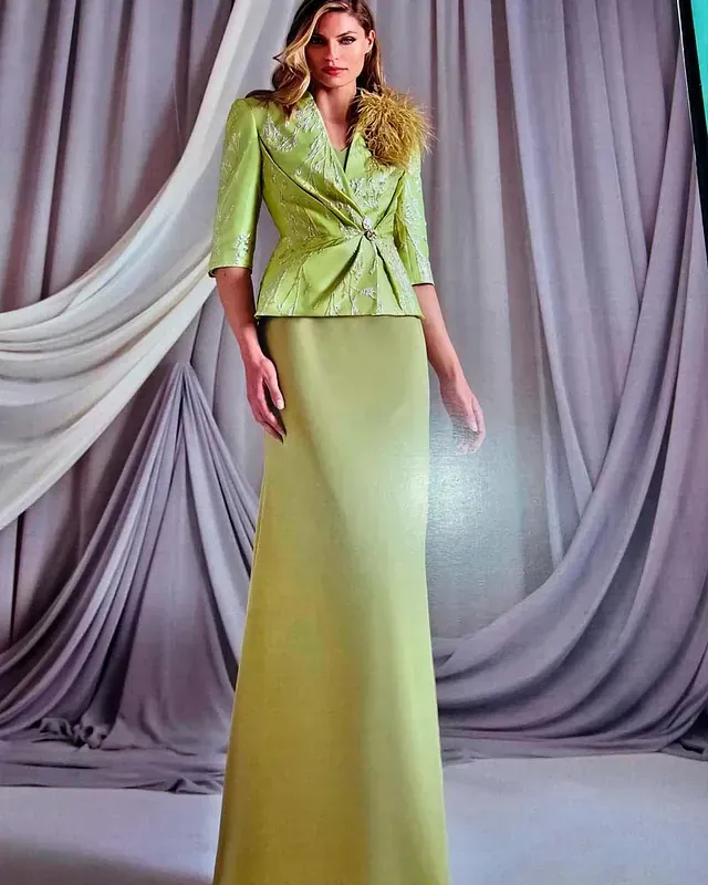 Una mujer con un vestido y una chaqueta verdes está parada frente a una cortina.