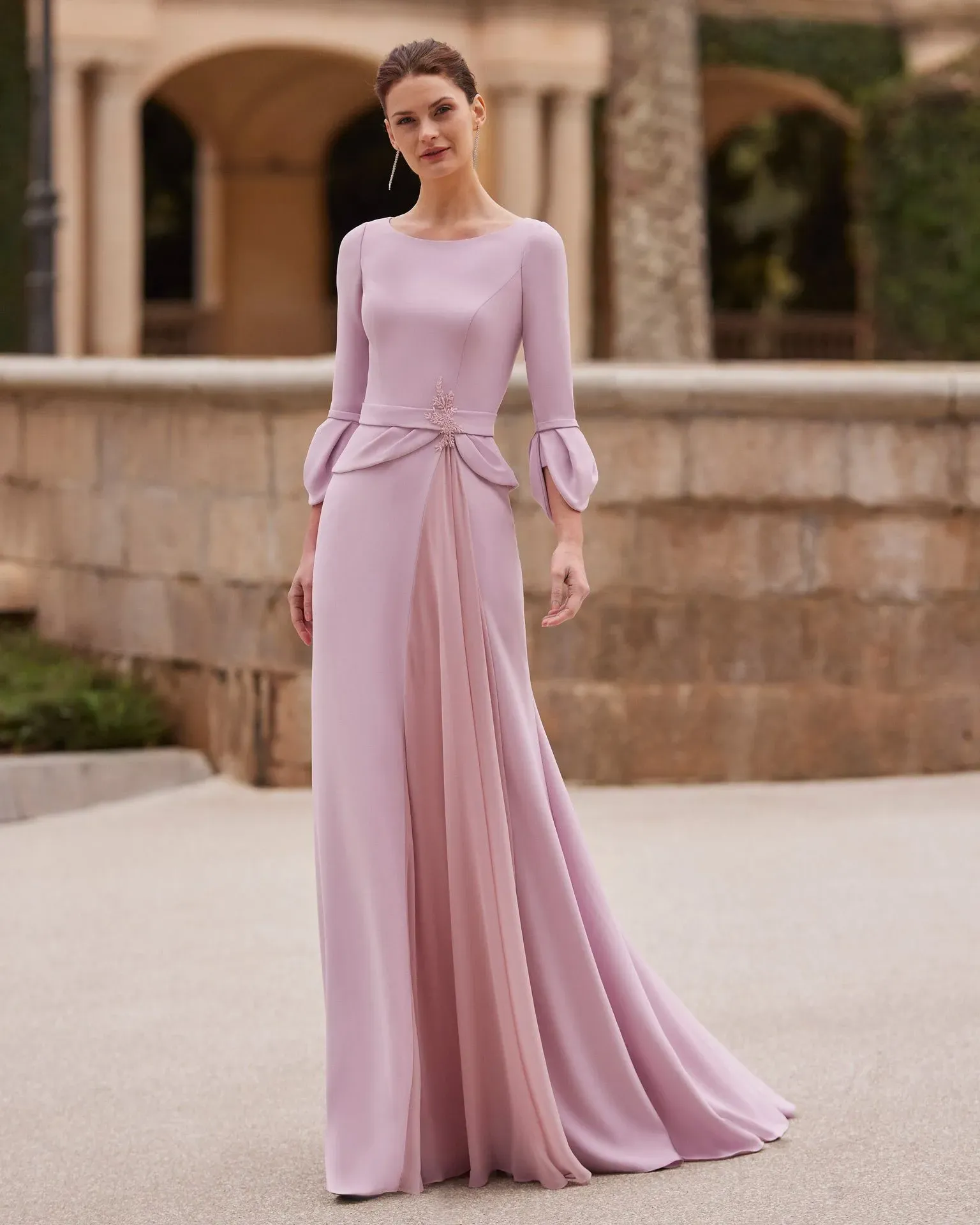 Una mujer lleva un vestido largo rosa con mangas largas.