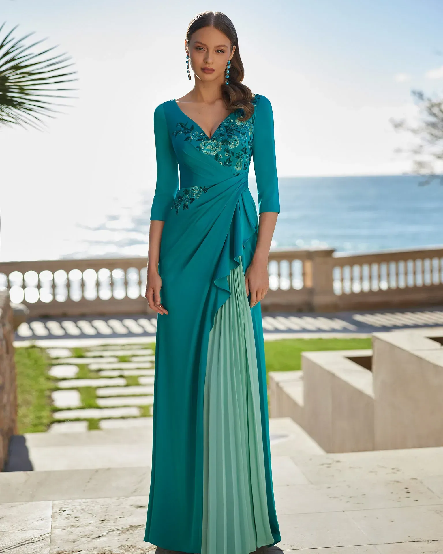 Una mujer con un vestido largo azul está parada frente al océano.