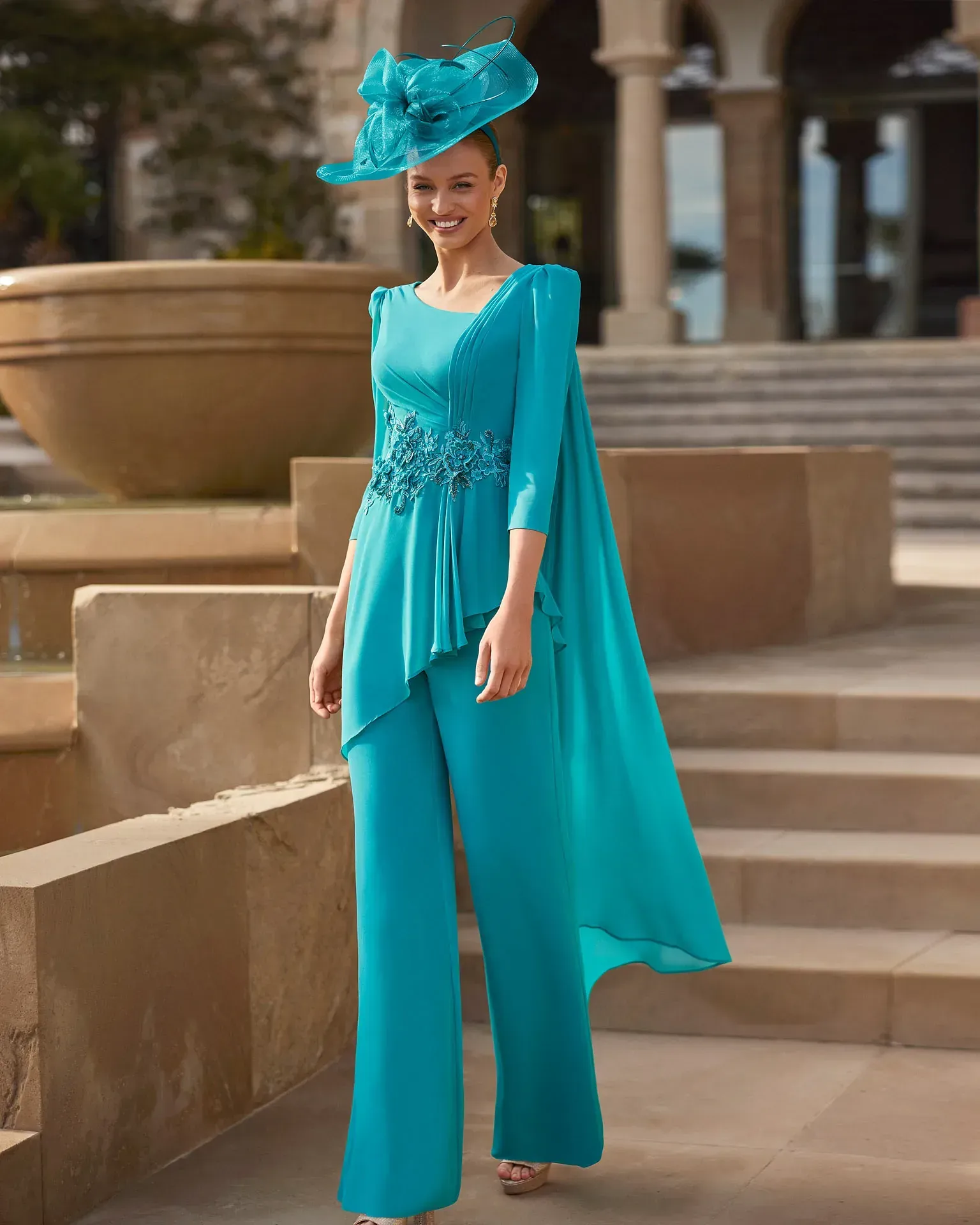 Una mujer con un vestido azul y un sombrero está parada junto a una fuente.