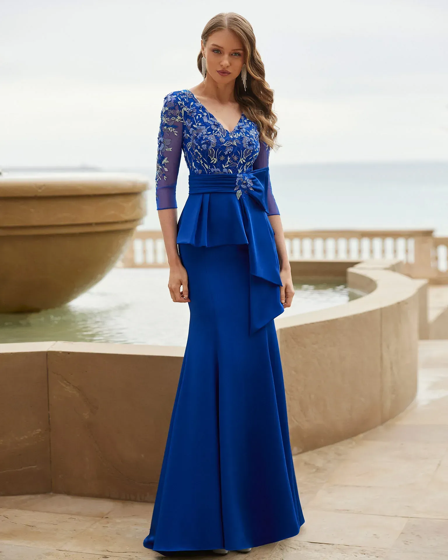 Una mujer con un vestido azul está parada frente a una fuente.