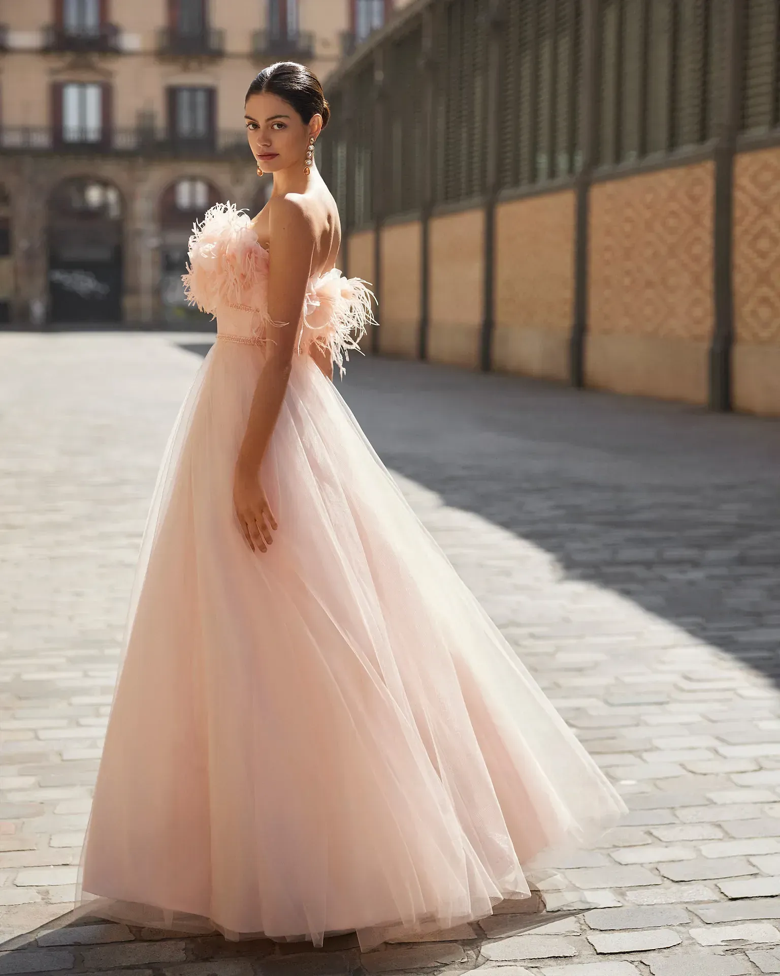 Una mujer con un vestido largo rosa está parada en una acera.