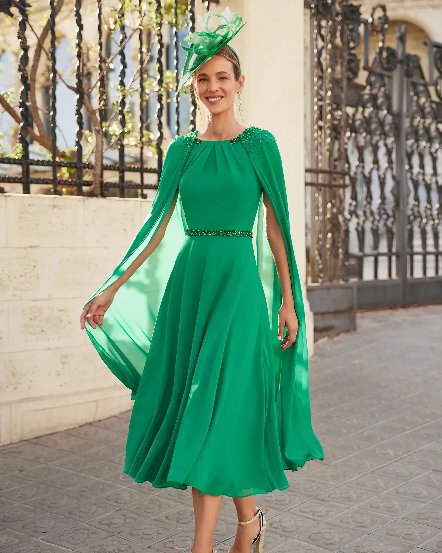 Una mujer lleva un vestido verde con una capa y un sombrero.
