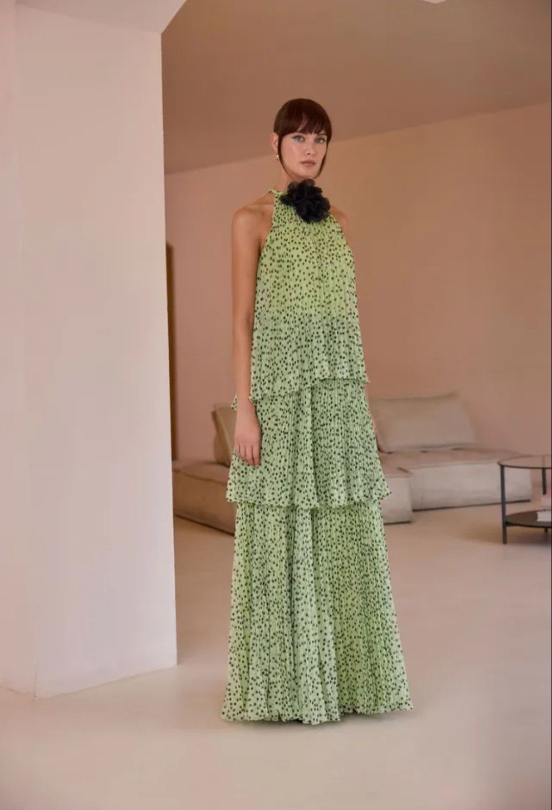 Modelo con un vestido verde estampado de volantes de pie en una habitación minimalista de color beige.