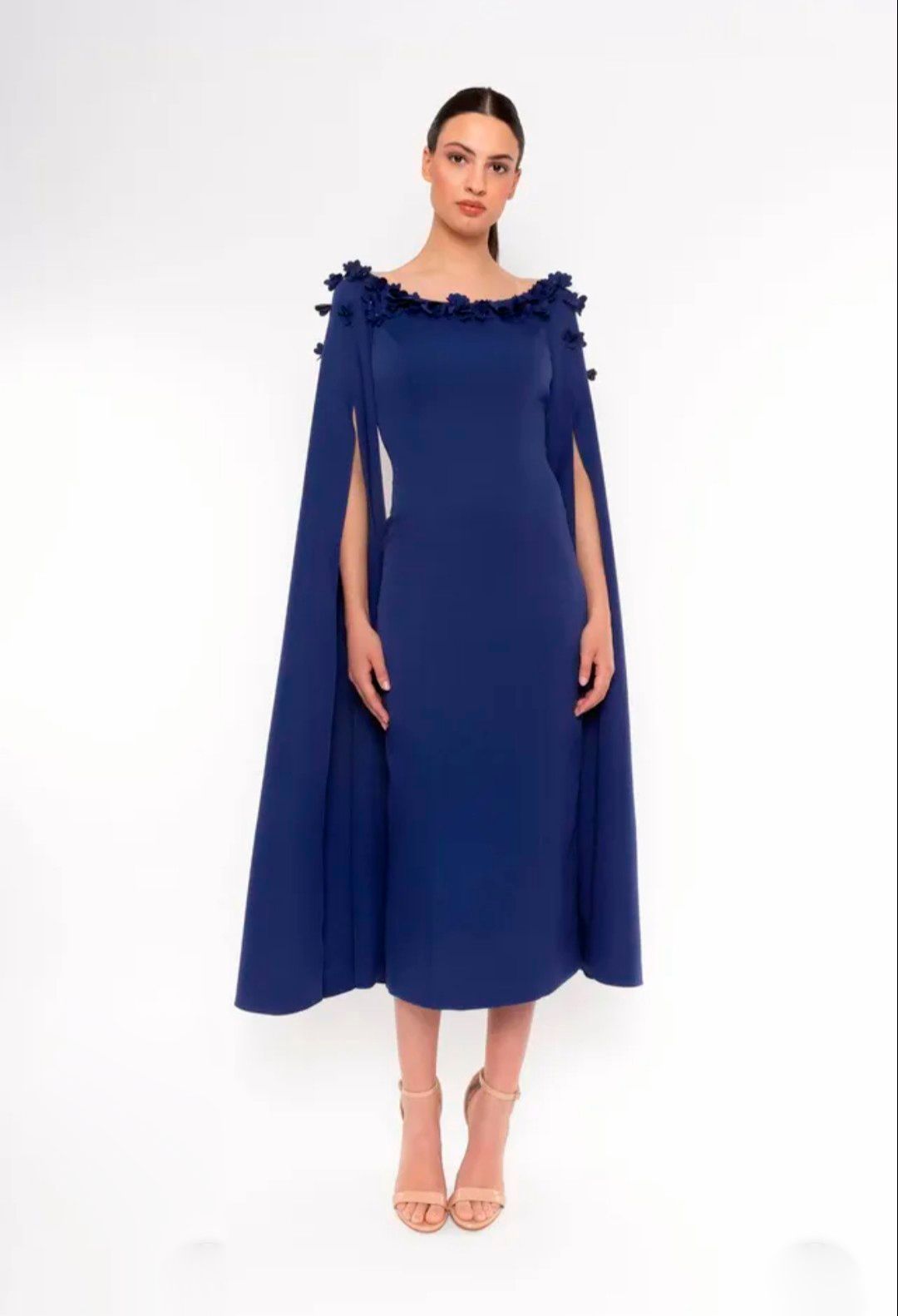 Mujer con un vestido capa azul marino y tacones color nude, de pie sobre un fondo blanco.