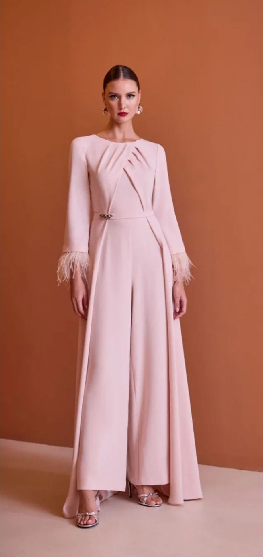 Vestido largo plisado de color rosa empolvado con mangas largas, lucido por una modelo sobre un fondo terracota.