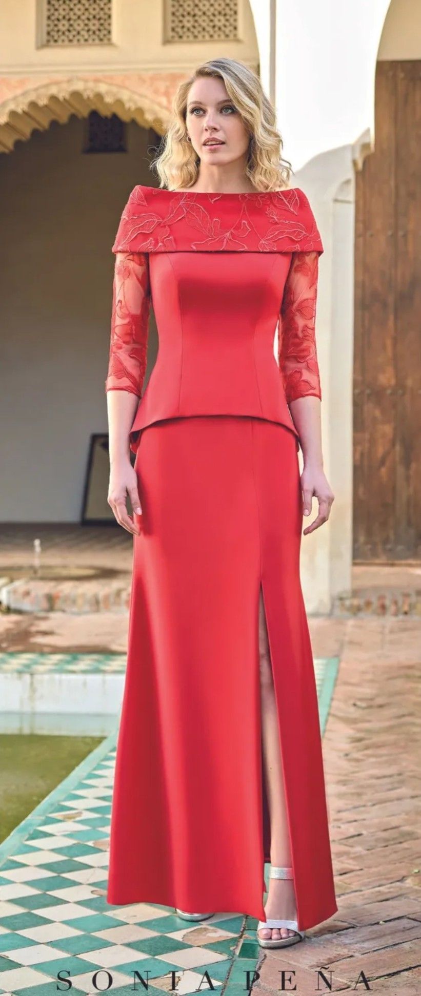 Mujer con un vestido rojo sin tirantes de pie junto a una piscina en un patio ornamentado.