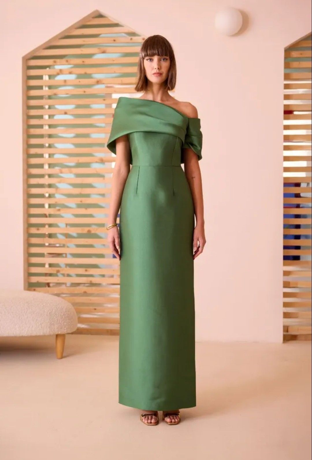 Mujer con un vestido verde sin hombros de pie en un estudio minimalista con decoración de arco de madera