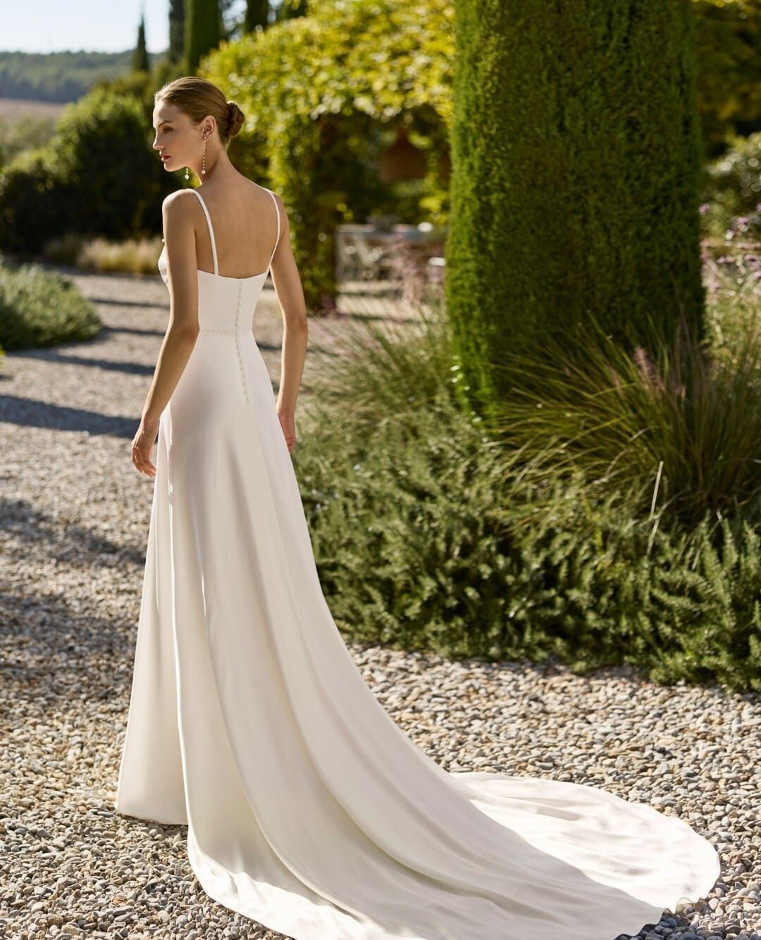 Novia con un vaporoso vestido blanco caminando al aire libre por un sendero del jardín.