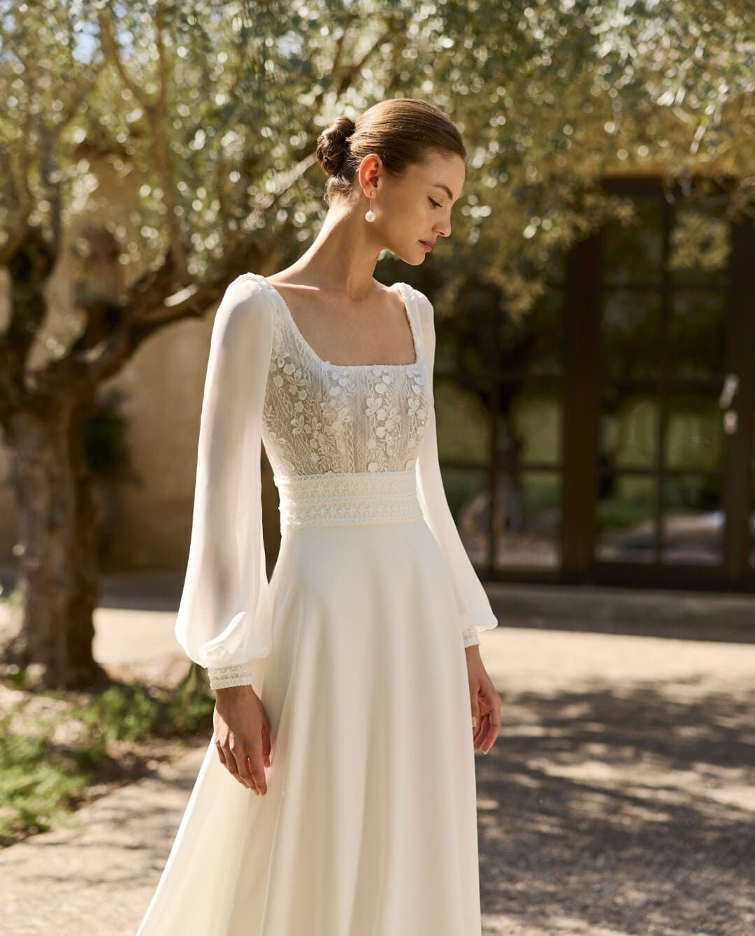 Vestido blanco de manga larga con corpiño bordado con cuentas, usado al aire libre en un sendero soleado.