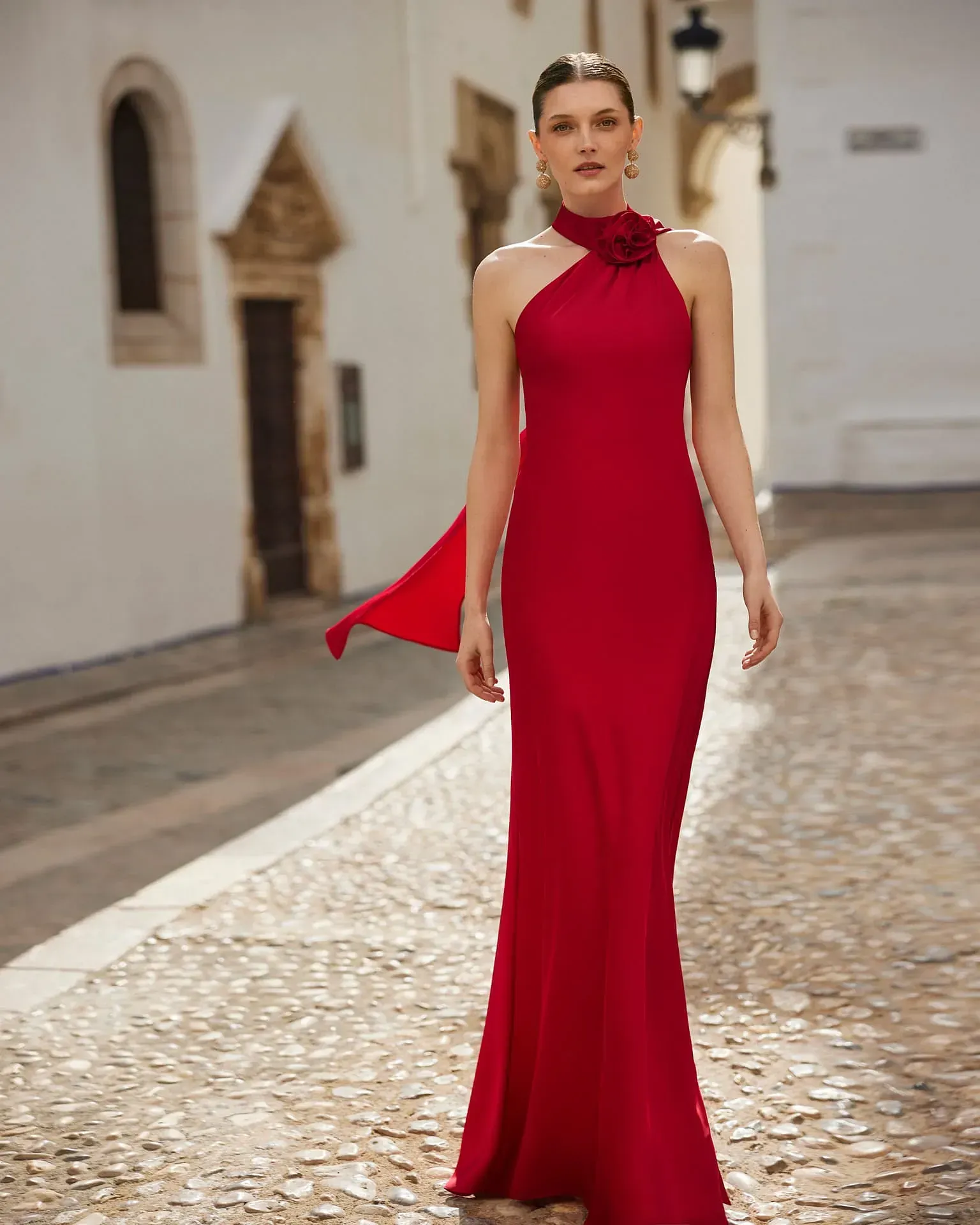 Una mujer con un vestido largo rojo camina por una calle adoquinada.