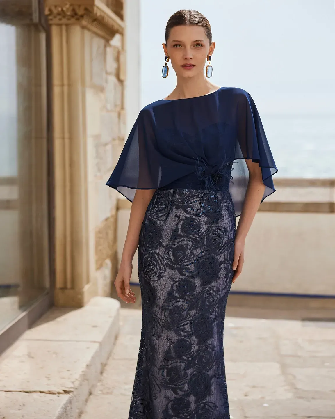 Una mujer lleva un vestido largo azul y pendientes.