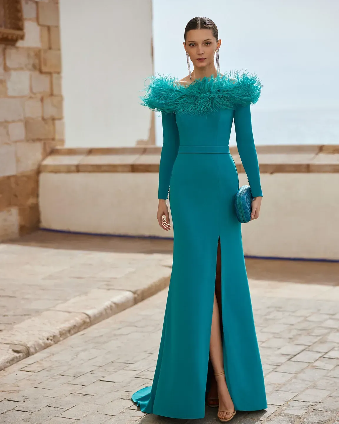 Una mujer lleva un vestido largo verde con plumas en los hombros.