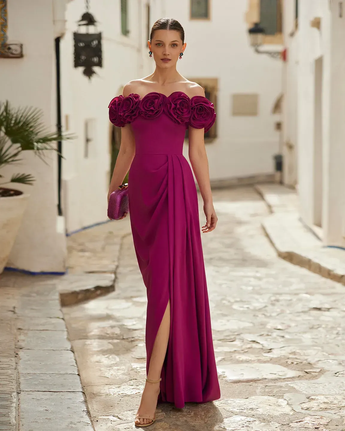 Una mujer lleva un vestido largo morado con flores en los hombros.