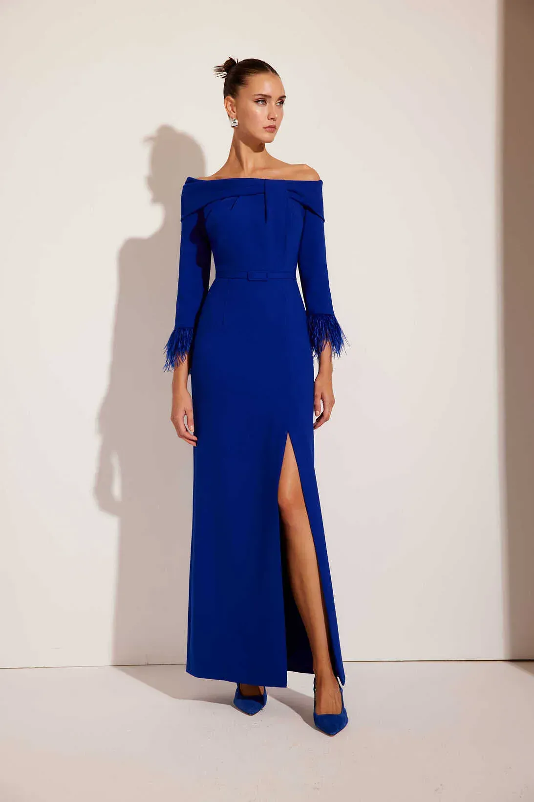 Una mujer lleva un vestido azul con hombros descubiertos y plumas en las mangas.