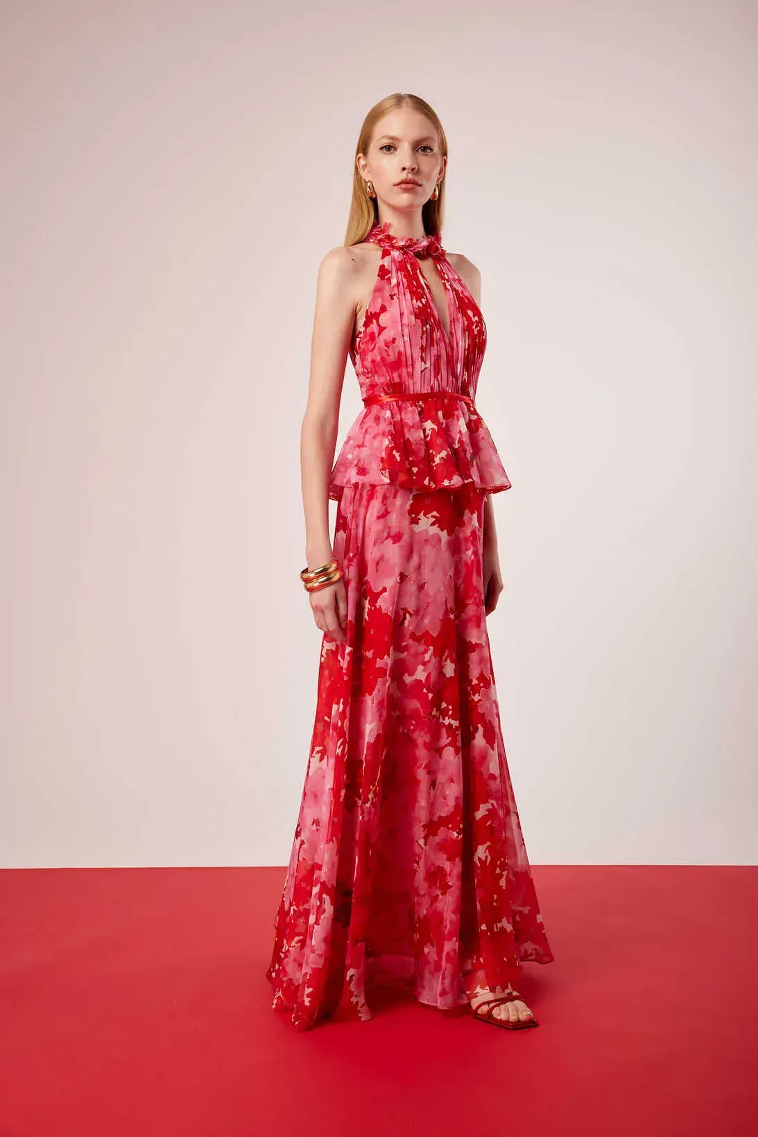 Una mujer con un vestido rojo está parada sobre una alfombra roja.
