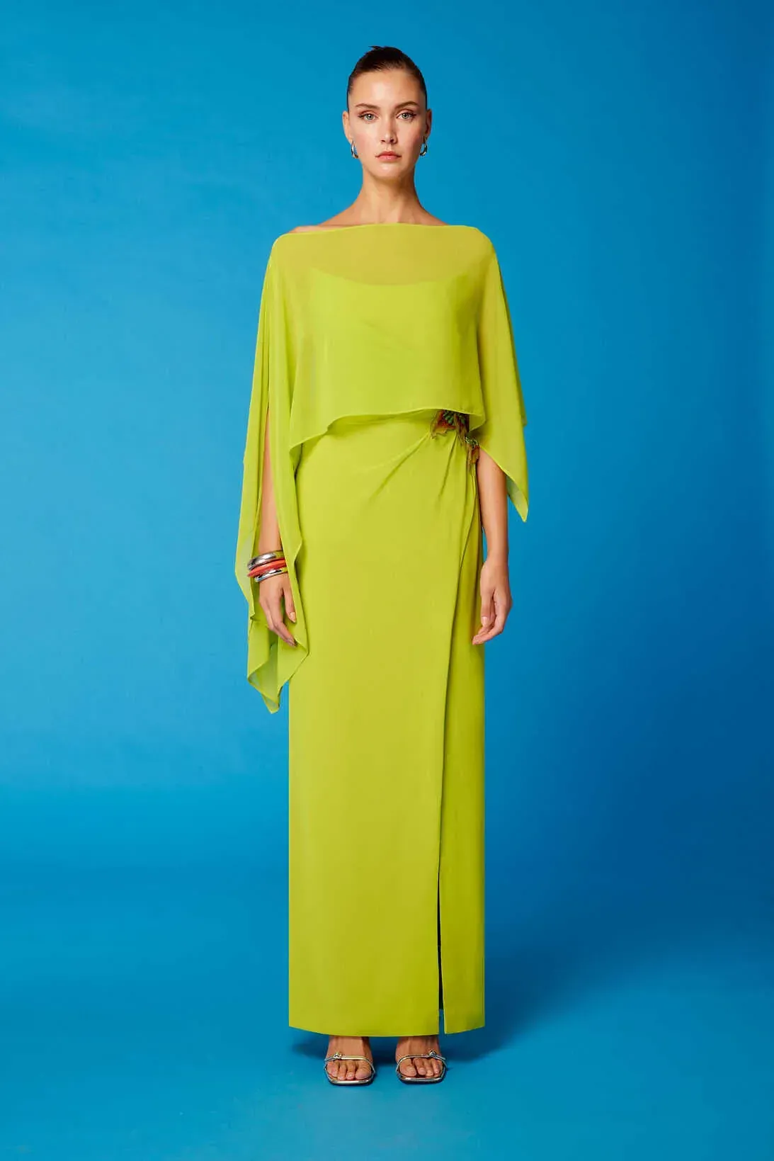 Una mujer lleva un vestido largo verde lima con una capa.