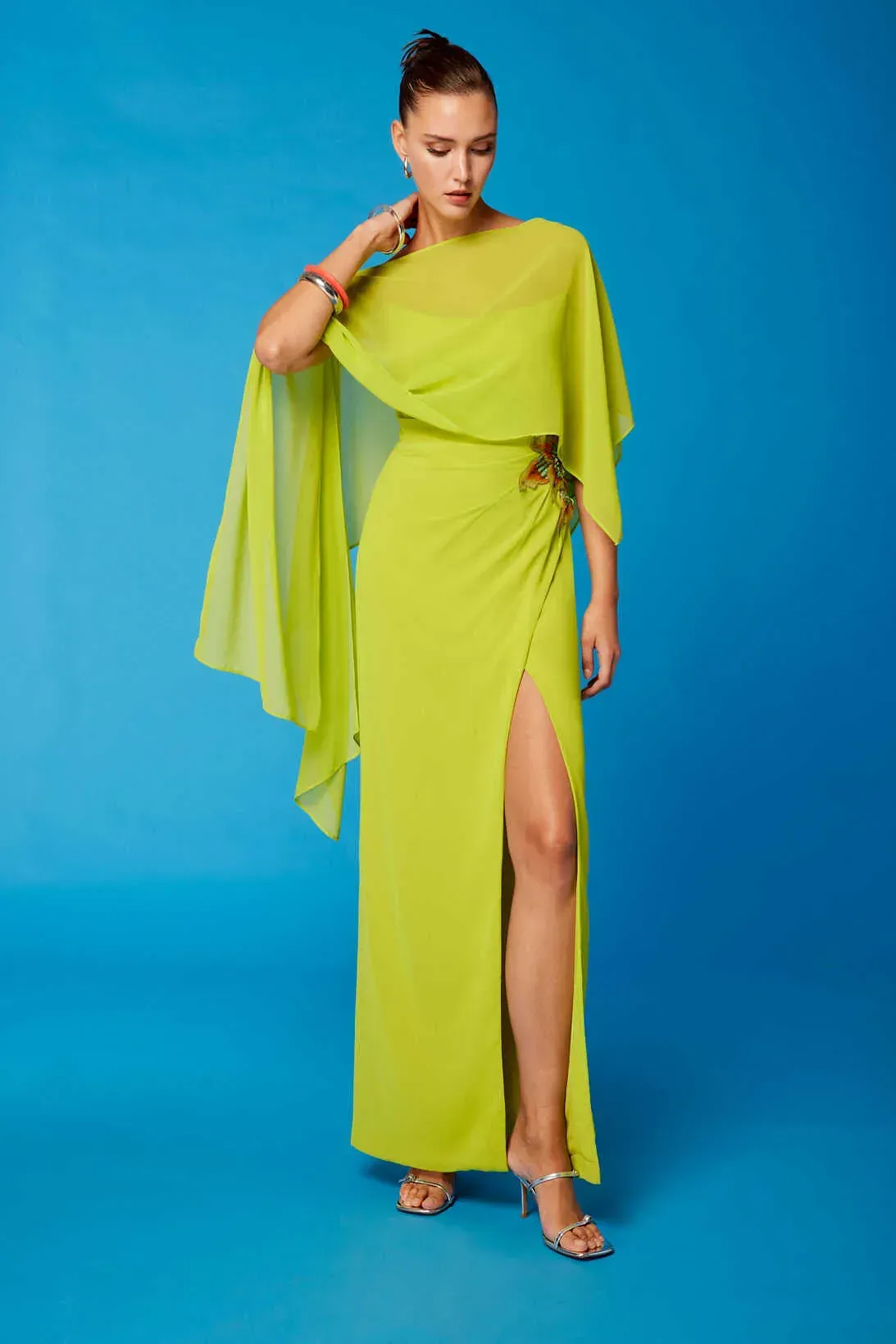 Una mujer lleva un vestido amarillo neón con una capa.