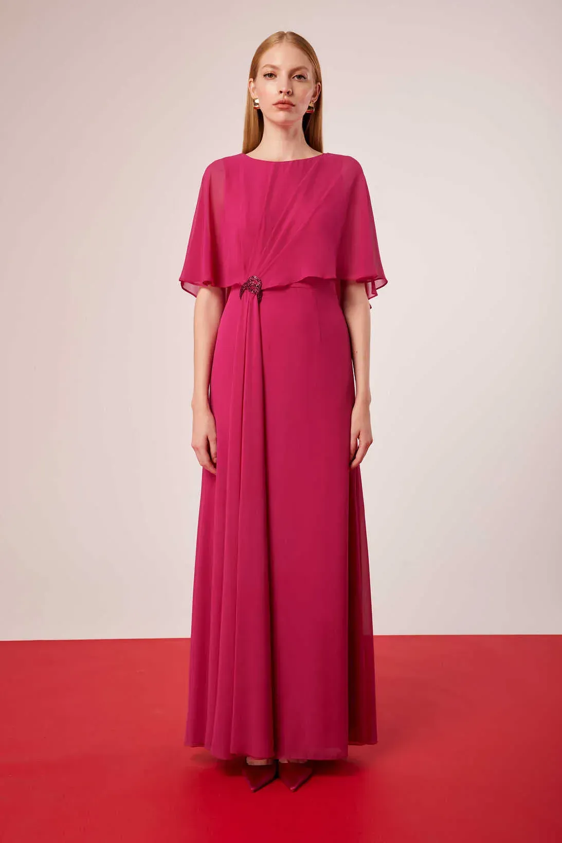 Una mujer con un vestido largo rosa está parada sobre una alfombra roja.